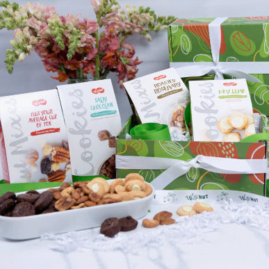 WataNut Assorted Nuts and Cookies gift box featuring Salty Chocolate and Keylime Shortbread cookies and Roasted Rosemary Deluxe Mixed Nuts. In our signature green gift box with white ribbon and a white dish in foreground holding assorted cookies and nuts