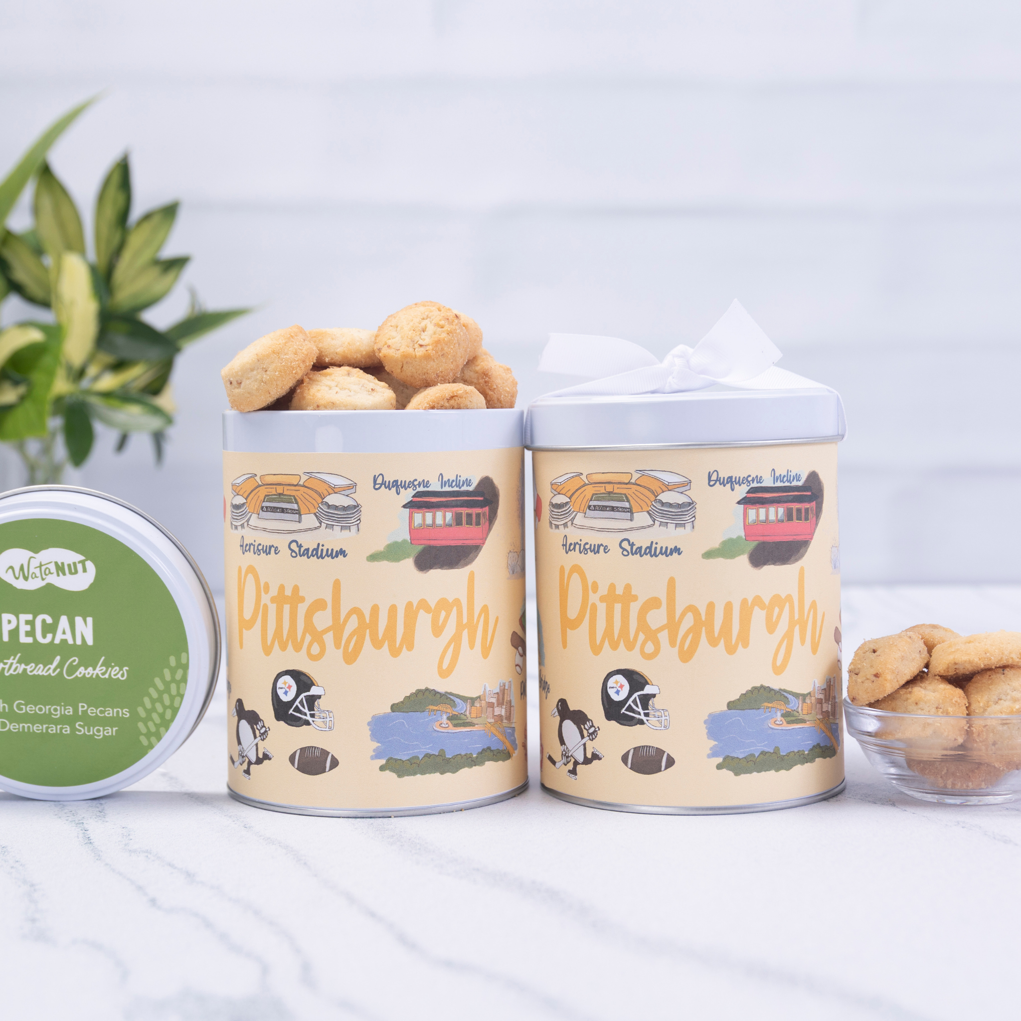 Two cylindrical Pittsburgh-themed cookie tins with pecans on a light background
