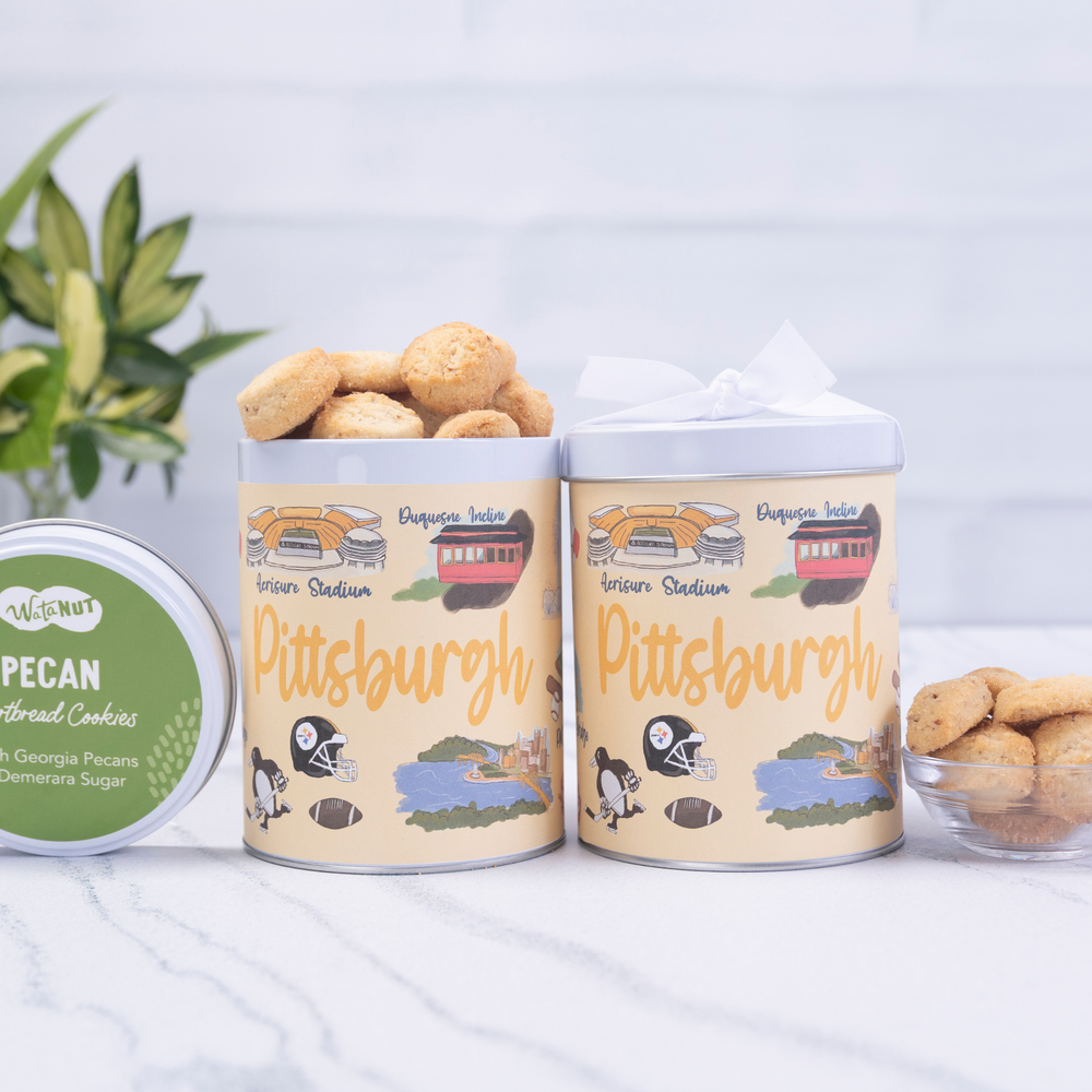 Two cylindrical Pittsburgh-themed cookie tins with pecans on a light background