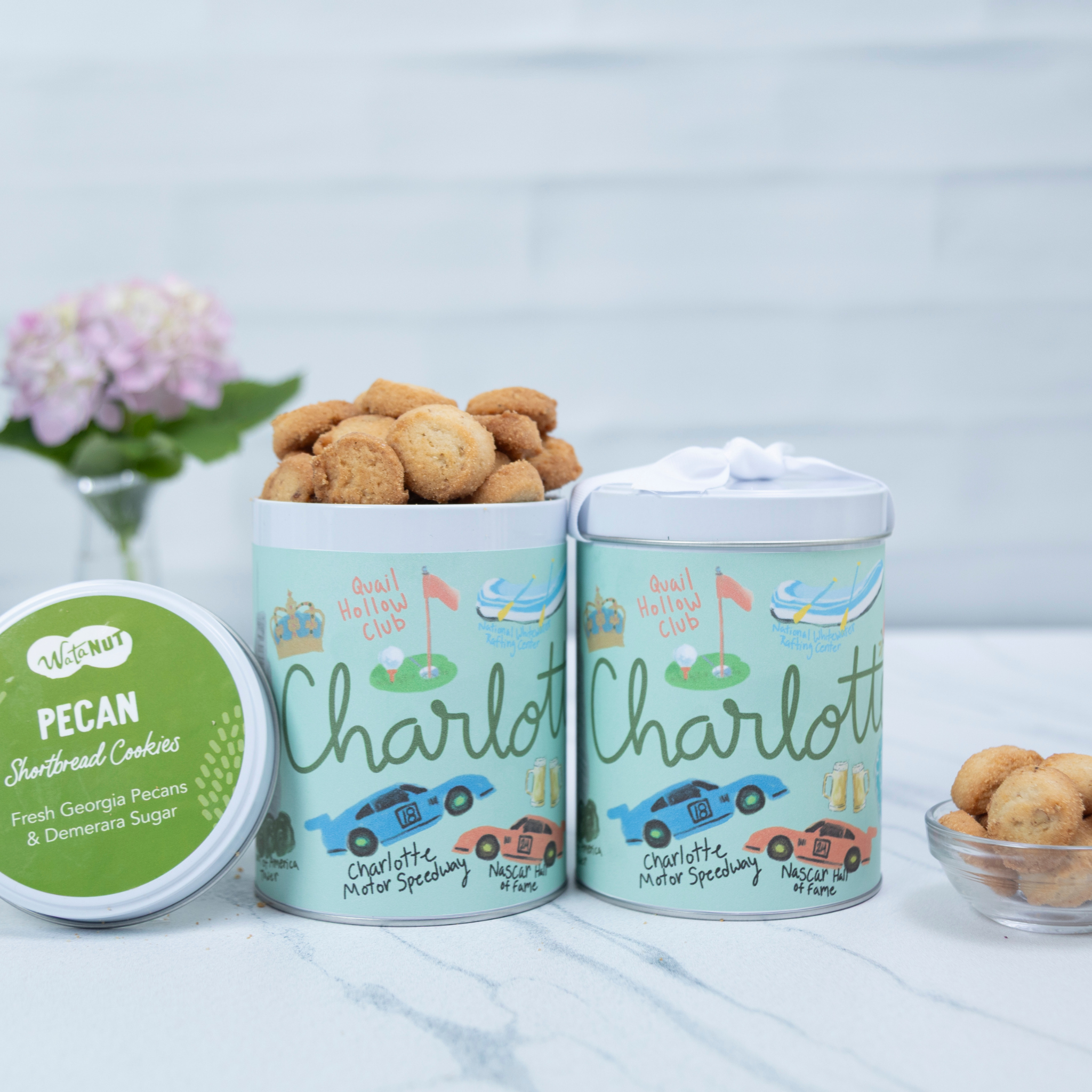 Two containers of Charlotte cookies with a small bowl of cookies on a light surface.